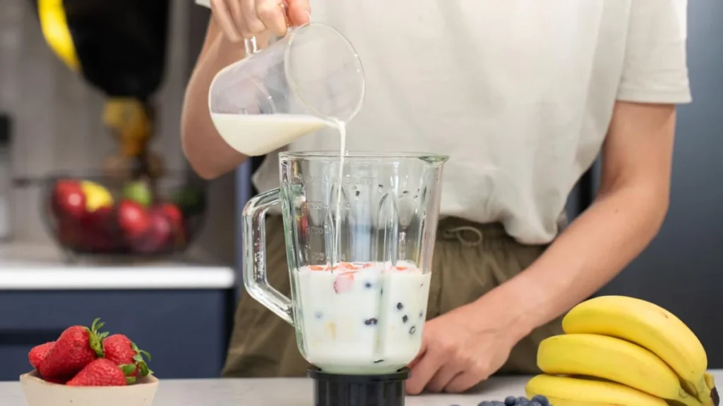 Smoothie Tips and Ingredients: The Ultimate Guide to Perfect Blends Every Time 4 Woman pouring milk into blender with berries and fruits. Fresh berry smoothie preparation