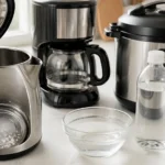 Electric kettle with white limescale buildup next to a drip coffee maker and Instant Pot, with a bottle of white vinegar ready for descaling on a bright kitchen counter